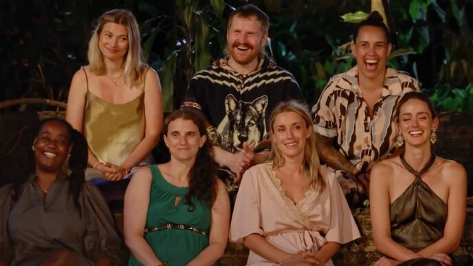 Group of seven diverse reality TV contestants smiling and laughing