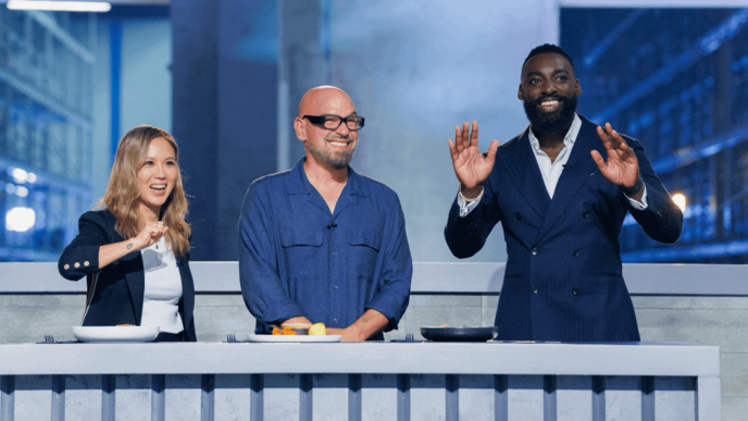 Three people stand behind a gray table, with the person on the right gesturing